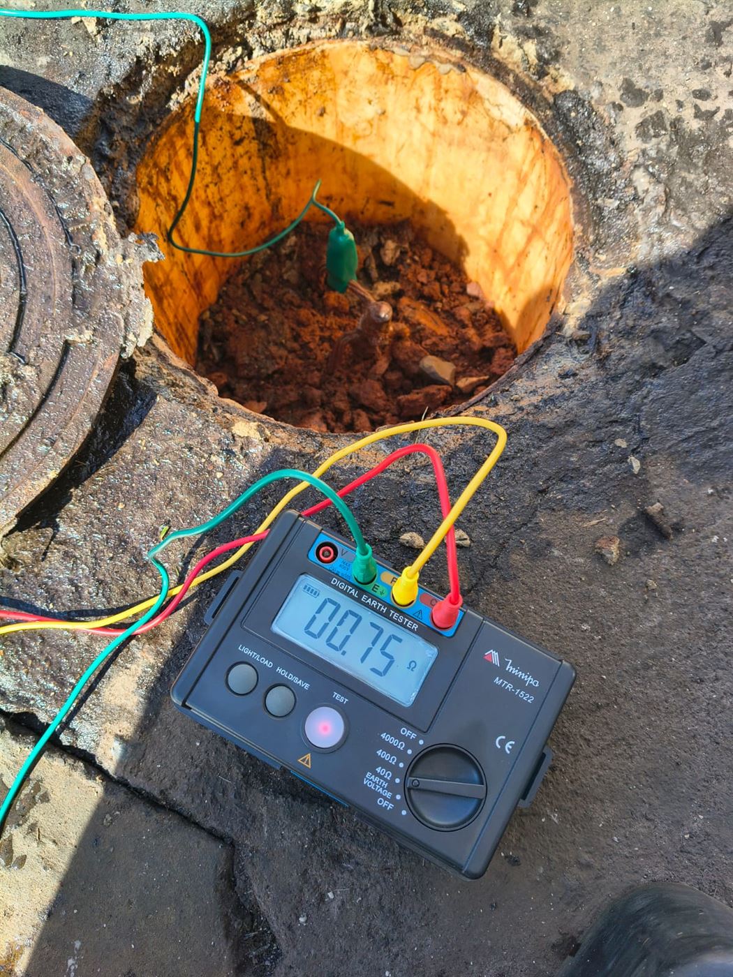 Terrômetro digital apoiado na borda da caixa de inspeção, com a leitura de 0,75 ohm no visor