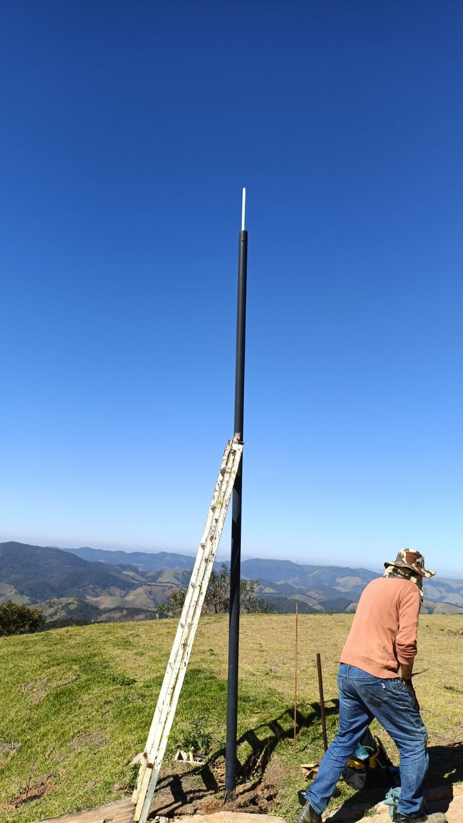 Mastro captor instalado em cota alta de pasto, com a serra ao fundo e a escada apoiada